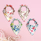 Four floral-patterned baby bibs on a pink background with pearls.