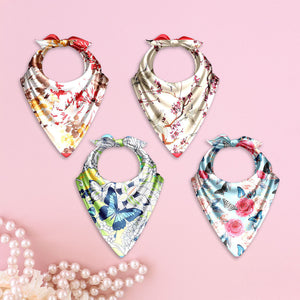 Four floral-patterned baby bibs on a pink background with pearls.
