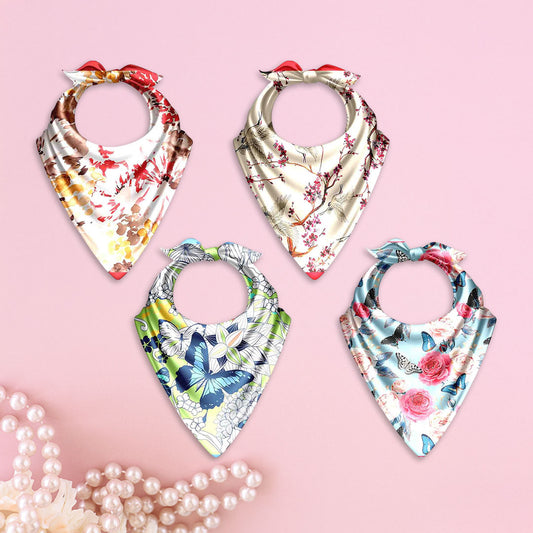 Four floral-patterned baby bibs on a pink background with pearls.