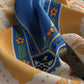 Colorful fabric with a blue pattern featuring flowers and geometric shapes on a multicolored background.