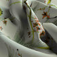 Floral and bird patterned fabric with green, orange, and black colors on a white background.